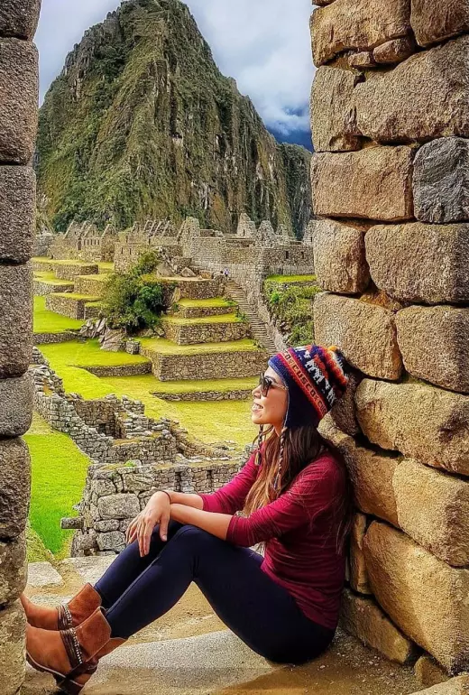 Turista con gorro y lentes de sol disfrutando la vista de la ciudadela de Machu Picchu