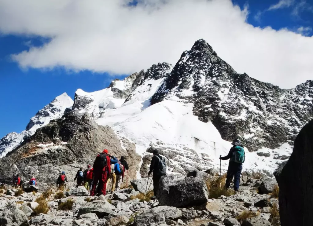 Grupo de trekkers con casacas de capas y bastones cruzando un paso de montaña nevado en los Andes